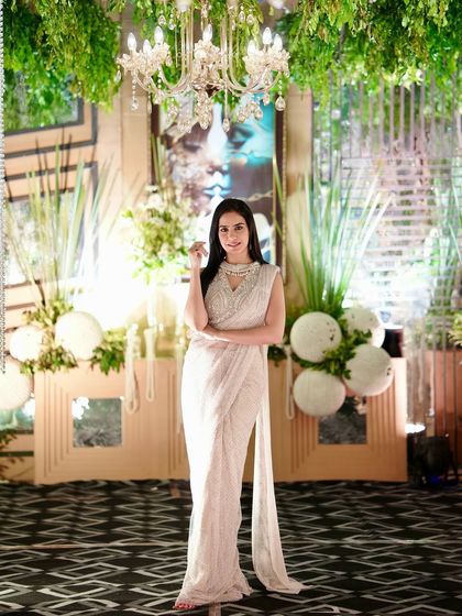 A full-length shot of the white saree, showing its complete silhouette against a beautifully decorated event backdrop.