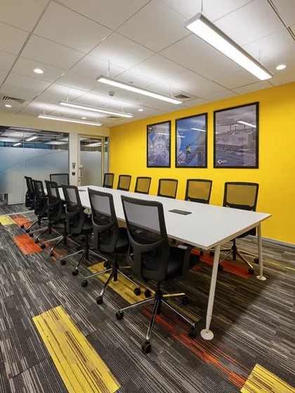 A bright and cheerful boardroom with a sunny yellow accent wall. The carpet tiles have a corresponding yellow and grey pattern, tying the whole room together.