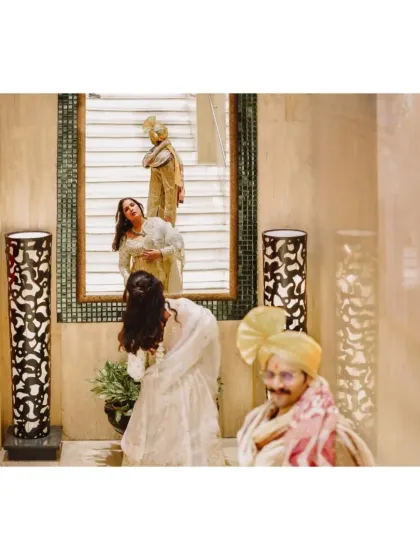 A creative and artistic shot using reflections. The groom waits while the bride is captured in multiple reflections, creating a layered and interesting composition.