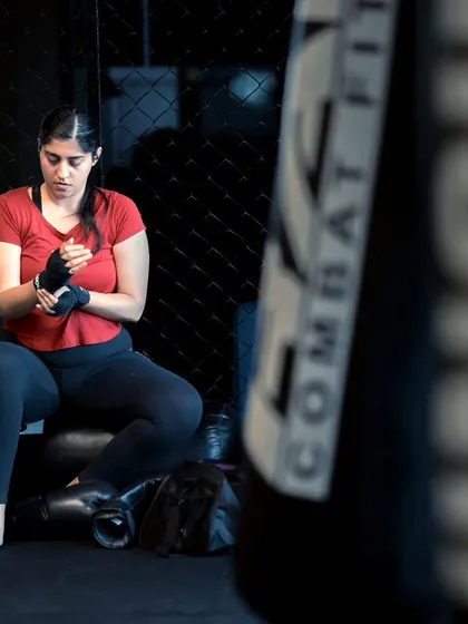 A female fighter sits and wraps her hands, focused on the training ahead.
