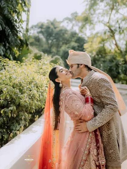 A romantic kiss shared by the newlyweds. This candid shot, set against a natural green backdrop, feels both intimate and joyful.