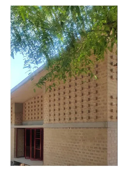 The textured brick facade seen from below, with a neem tree branch in the foreground. This perspective emphasizes the building's verticality and the natural materials used.