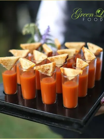A comforting classic reimagined. We serve creamy tomato soup in shot glasses, garnished with a miniature grilled cheese sandwich triangle. It's a playful and nostalgic appetizer that everyone loves.