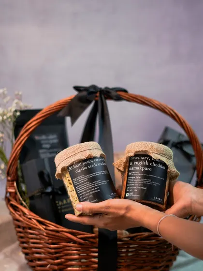 Choosing the perfect gift is easy with our customisable hampers. Here, we are holding jars of our popular basil pesto and rosemary namakpare, ready to be added to a bespoke wicker basket hamper.
