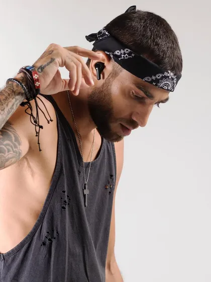 This studio shot for a tech brand highlights the product in a lifestyle context. The model's edgy styling with a bandana and tattoos contrasts with the clean, modern design of the earbuds, showing the product's appeal to a cool, urban demographic.