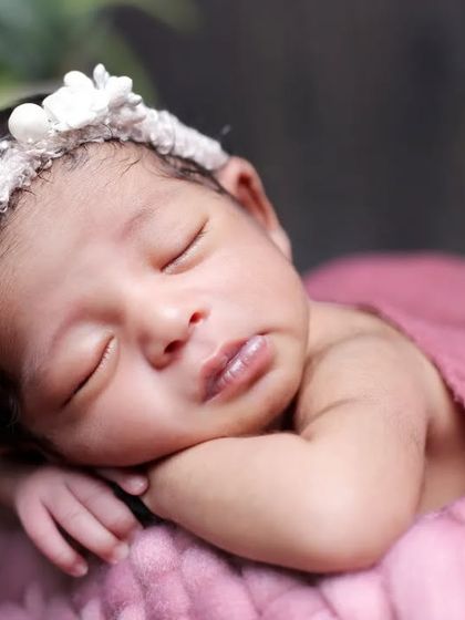 A beautiful close-up shot focusing on the newborn's face. The soft pink wrap and floral headband complement her delicate features perfectly.