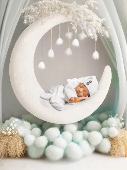 A winter-themed moon setup, with the baby in a cute bear hat sleeping on a white moon surrounded by soft, snow-like pom-poms.