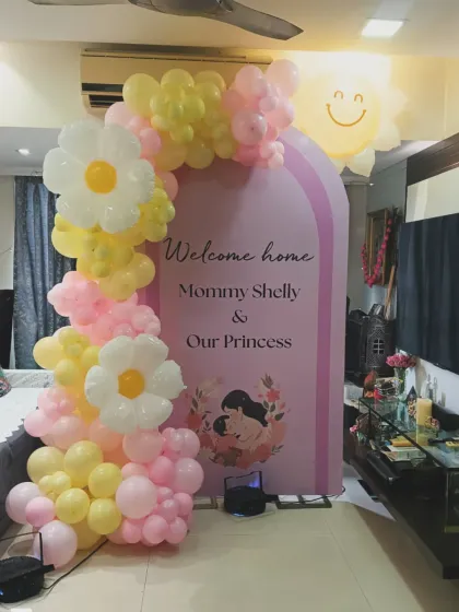 A bright and cheerful welcome home decoration for "Mommy Shelly & Our Princess". The design uses sunny yellow and pink balloons, with cute daisy and sun accents to create a happy and vibrant setting.
