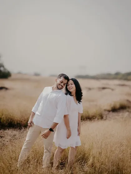 A wide shot showing the couple's joyful interaction in a beautiful, open field. Their happiness is the central theme of this natural pre-wedding portrait.