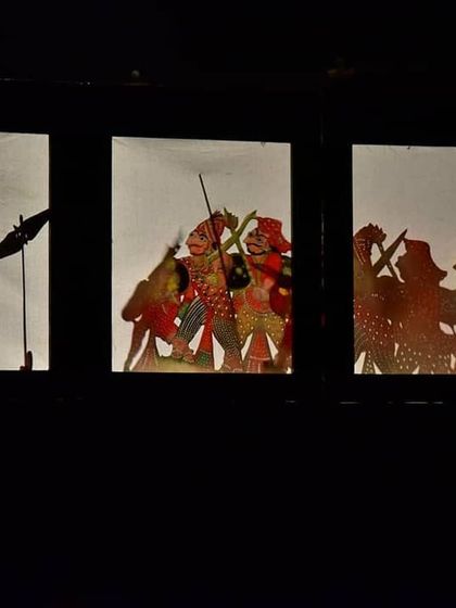 A closer look at the shadow puppets, depicting a scene of conflict or action. The silhouettes are crafted to be clear and dynamic, telling a story through form and movement alone.