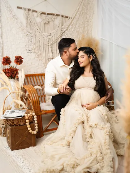 A tender moment during a boho-themed studio maternity shoot. The warm, earthy tones and natural textures create a cozy atmosphere, perfectly framing the couple's loving anticipation.