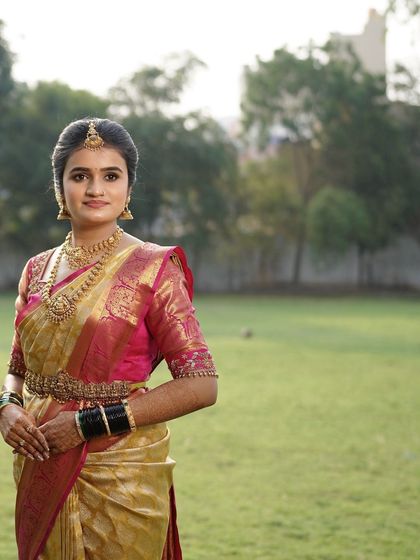 A beautiful outdoor shot of this bride on her wedding day. The natural light highlights the dewy finish of her makeup and the vibrant colors of her pink and gold silk saree.