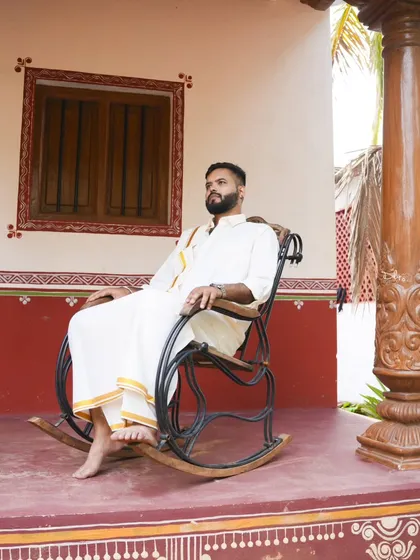 A classic portrait of the groom-to-be in a traditional white dhoti and shirt, seated on a rocking chair. This shot has a timeless, old-world charm.