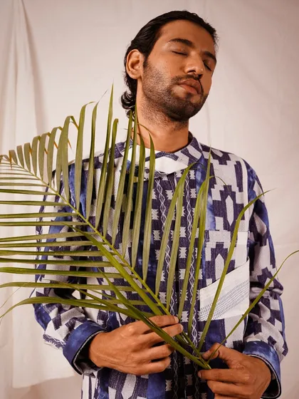 An artistic shot where the model holds a palm leaf, adding a natural, organic element that contrasts with the geometric print of the shirt. This adds a layer of storytelling to the lookbook.