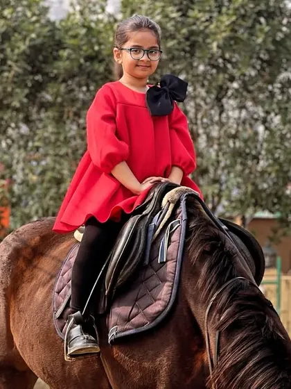 Dressed in a bright red dress, this young girl poses elegantly on her horse, creating a beautiful and stylish children's portrait.