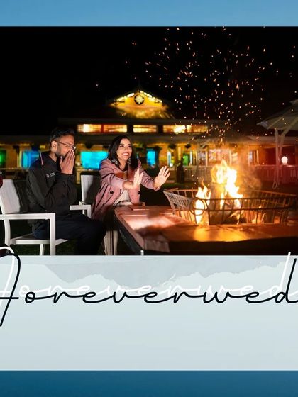 A wider shot of the bonfire scene, capturing the full ambiance of the location. The sparks flying into the night sky add a dynamic and magical element to this romantic pre-wedding moment.