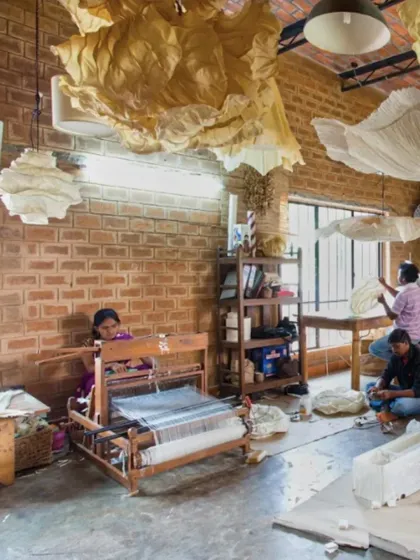 The interior of the Oorjasi paper-making workshop. The space is a hive of activity, with high ceilings and large windows providing ample light for the artisans at work. The exposed brick walls add to the studio's rustic, creative character.