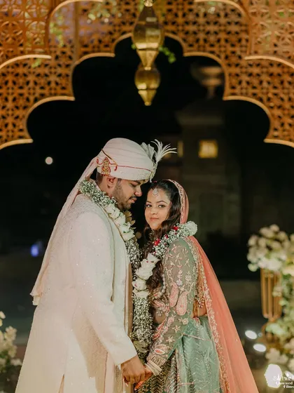 A quiet moment between the couple after the ceremony. The soft lighting and intricate background details of the mandap create a romantic and intimate portrait.