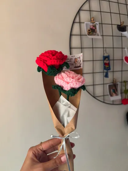 A simple yet classic gift: a mini bouquet of one red and one pink crochet rose, wrapped in brown paper.