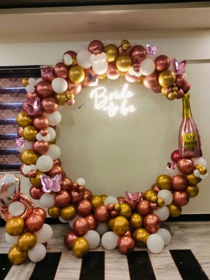 This elegant indoor balloon ring is perfect for a bride-to-be celebration. The combination of metallic rose gold, gold, and white balloons, along with a champagne bottle foil balloon, creates a chic and festive photo corner.
