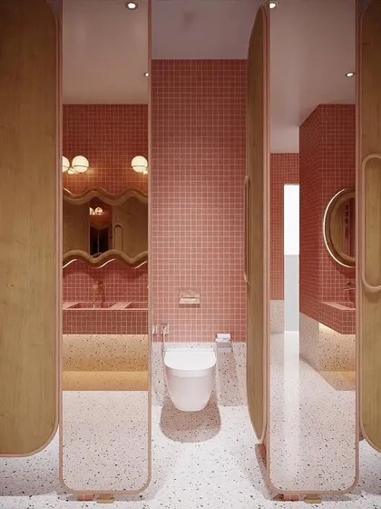 The entrance to the washroom stalls, featuring full-height mirrored doors with custom wood handles. The combination of pink mosaic tiles and terrazzo flooring creates a fun and luxurious feel.