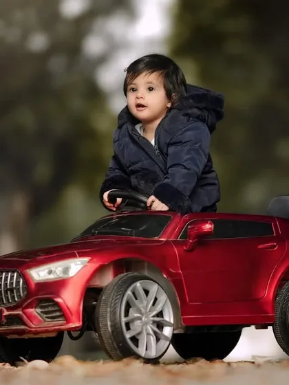 Looking up in wonder from the driver's seat. This little boy in his red toy car is captivated by the world around him during his outdoor shoot.