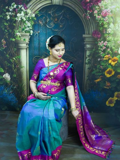 An elegant, seated portrait of a mom-to-be in a traditional blue and purple silk saree in our studio.