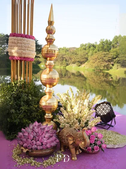 Details from a 'Pink Paradise' wedding, featuring tall brass decor pieces, lotus buds, and a brass elephant, all set against a stunning lakeside view.