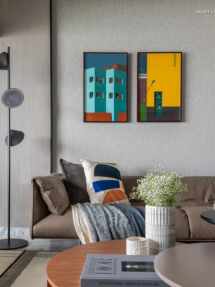 A detail shot of the art-filled living room, showcasing how playful designs and a minimalist vibe can coexist. The brown leather sofa is accented with colorful cushions and flanked by a modern floor lamp and vibrant paintings, reflecting the owner's personality.