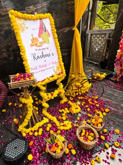 A detailed look at an entrance setup for a Haldi Mahotsav. I used a custom welcome sign, flower petals scattered on the floor, and small decorative props like a bicycle to create an inviting atmosphere.