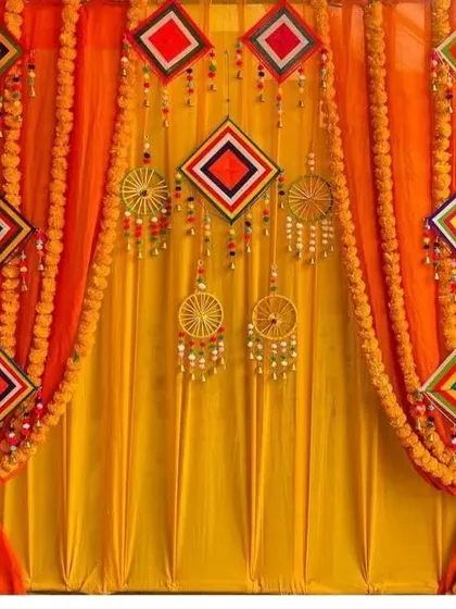 A traditional backdrop for a Haldi or Mehndi ceremony. I used bright orange and yellow curtains with marigold flower garlands and colorful diamond-shaped hangings for a completely traditional look.