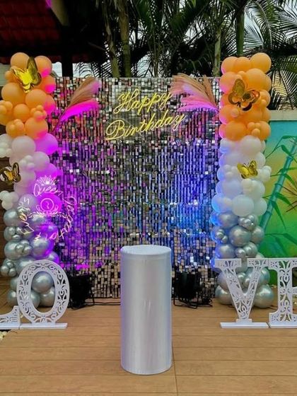 A vibrant outdoor setup with a sequin wall, "LOVE" marquee letters, and colorful balloon columns.