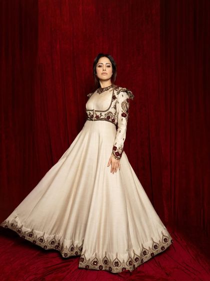 A dynamic full-length shot from the same series, capturing the beautiful flare of the Anarkali gown against the deep red backdrop.