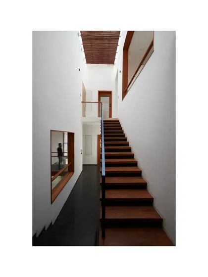 A narrow wooden staircase in the Vikas Residence, set against clean white walls. The design emphasizes simplicity and the natural beauty of the materials.