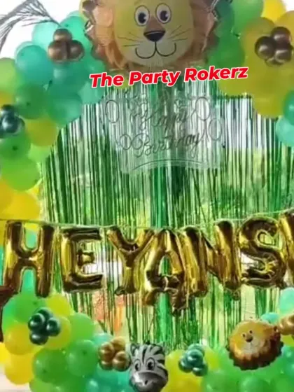 The main photo backdrop for the 5th birthday jungle party. The gold foil name balloons stand out against the green fringe and colorful balloon arch.
