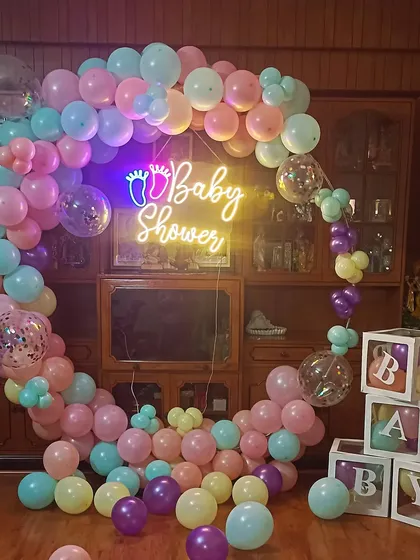 A beautiful baby shower setup with a pastel-colored balloon ring. The "Baby Shower" neon sign and "BABY" blocks make for a perfect photo corner.
