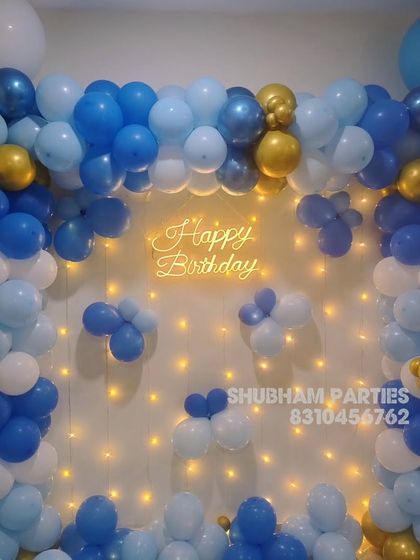 A dense wall of blue, white, and gold balloons with a "Happy Birthday" neon sign.