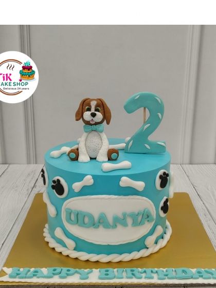 A cute and playful cake for a second birthday. This design features a fondant puppy with a bow tie, surrounded by edible bones and paw prints.