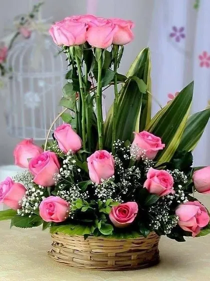 This two-tiered pink rose basket is a beautiful alternative to a standard bouquet. The arrangement is designed to be displayed on a table, making it a lovely gift for a home or office.