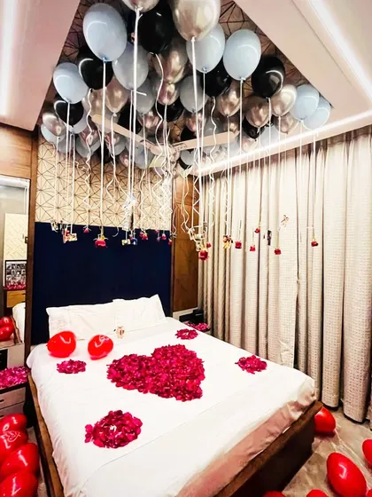 We transformed this bedroom for a romantic anniversary surprise. The decor includes red rose petals on the bed, heart-shaped red balloons, and silver and black balloons floating on the ceiling to create a memorable moment.