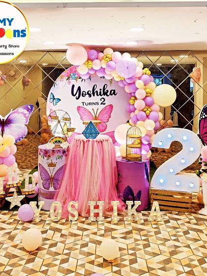 A breathtaking butterfly theme for a second birthday. This setup features a mirrored floor, a central tulle-draped table, large butterfly cutouts, and a pink and purple balloon arch, creating a truly magical atmosphere.