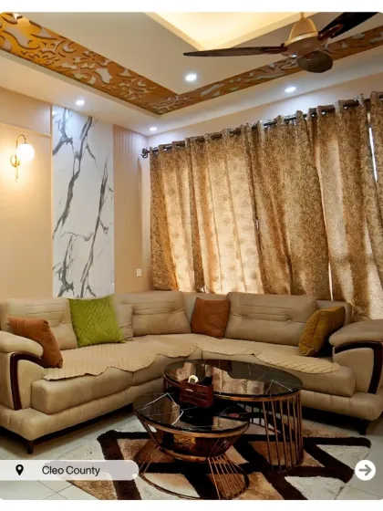 A living room that balances comfort and style. The beige sofa is complemented by intricate gold detailing on the false ceiling and a marble-textured accent wall.