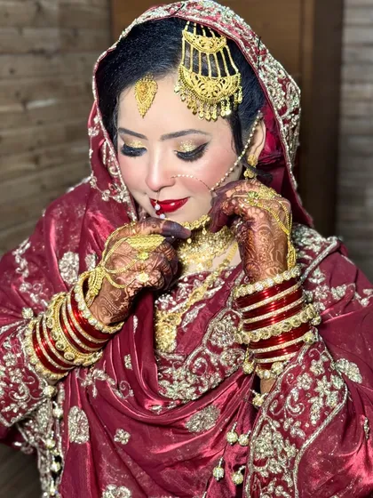 This bride is adjusting her nath, a classic moment on the wedding day. Her HD makeup features a bright red lip and golden glittery eyes, a timeless combination for a Nikkah ceremony.