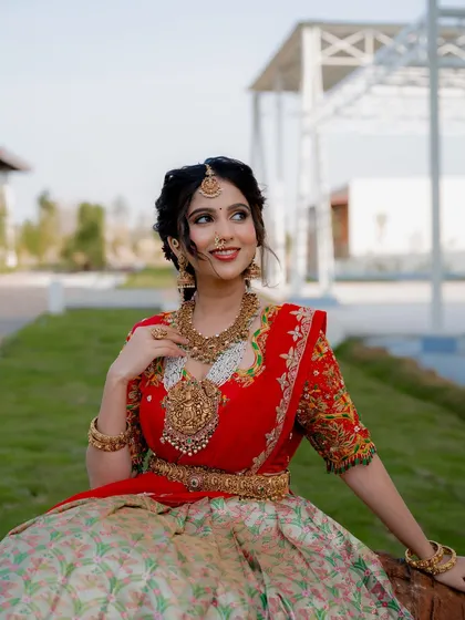 A joyful portrait of actress Niveditha Gowda seated in a garden. Her smile and the beautiful traditional attire create a bright and happy image.