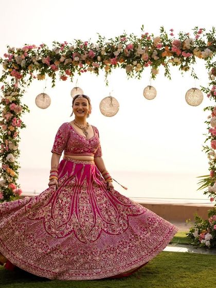 The bride twirls in her vibrant pink lehenga, creating a beautiful motion shot against the beachside floral mandap. A moment of pure bridal joy.