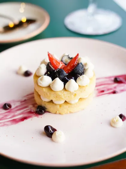 A beautifully plated mini cake with layers of sponge, cream, and fresh berries. The artistic smear of berry coulis on the plate adds a touch of fine-dining elegance.
