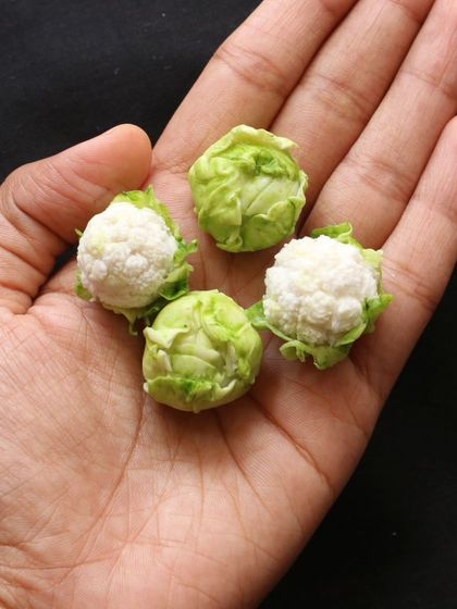 A hand holding four miniature cabbages and cauliflowers.