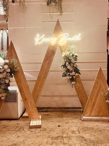 We specialize in creating elegant and memorable milestone celebrations. This custom-built "Kissing Booth" photo-op, featuring a neon sign and floral arrangements, served as a chic centerpiece for a 25th-anniversary party.