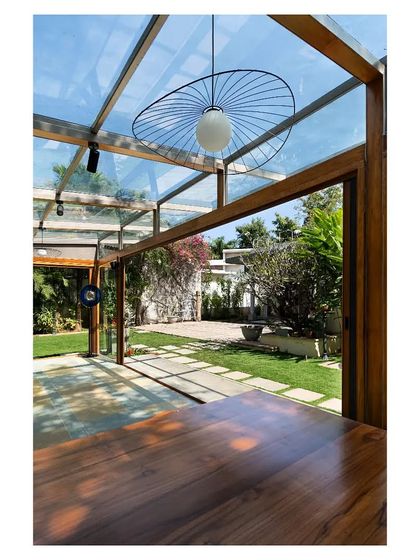 A modern pendant light hangs from the steel roof structure, its form echoing the organic shapes of the garden outside.
