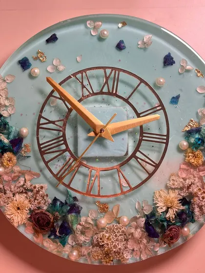 This 12-inch wall clock features a beautiful arrangement of preserved flowers against a soft blue background. The Roman numeral dial adds a touch of timeless elegance.